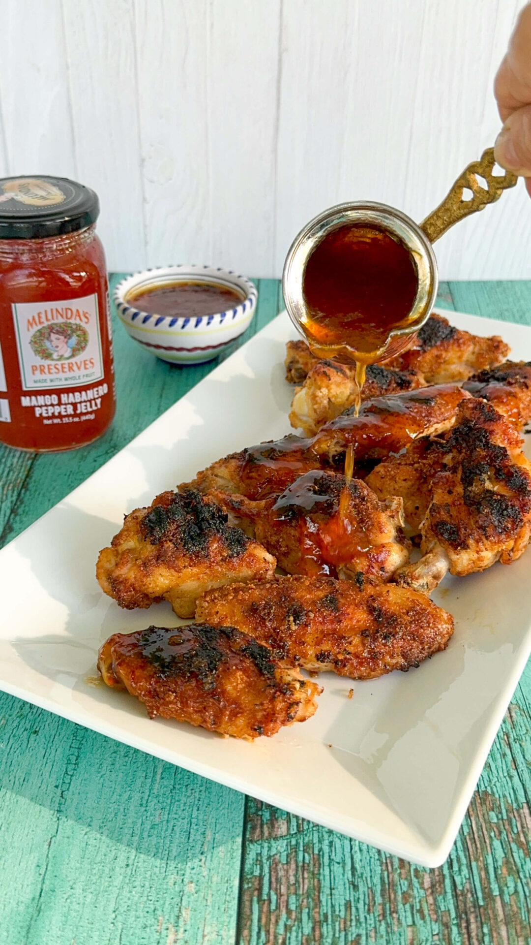 Picture of mango habanero wings on a white serving dish with mango habanero pepper jelly in the background. 