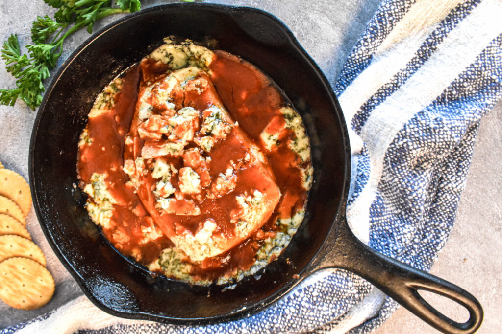 A cast iron skillet full of blue cheese smoked cream cheese dip with buffalo sauce.