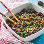 A bowl of egg roll in a bowl with two chopsticks sticking out.