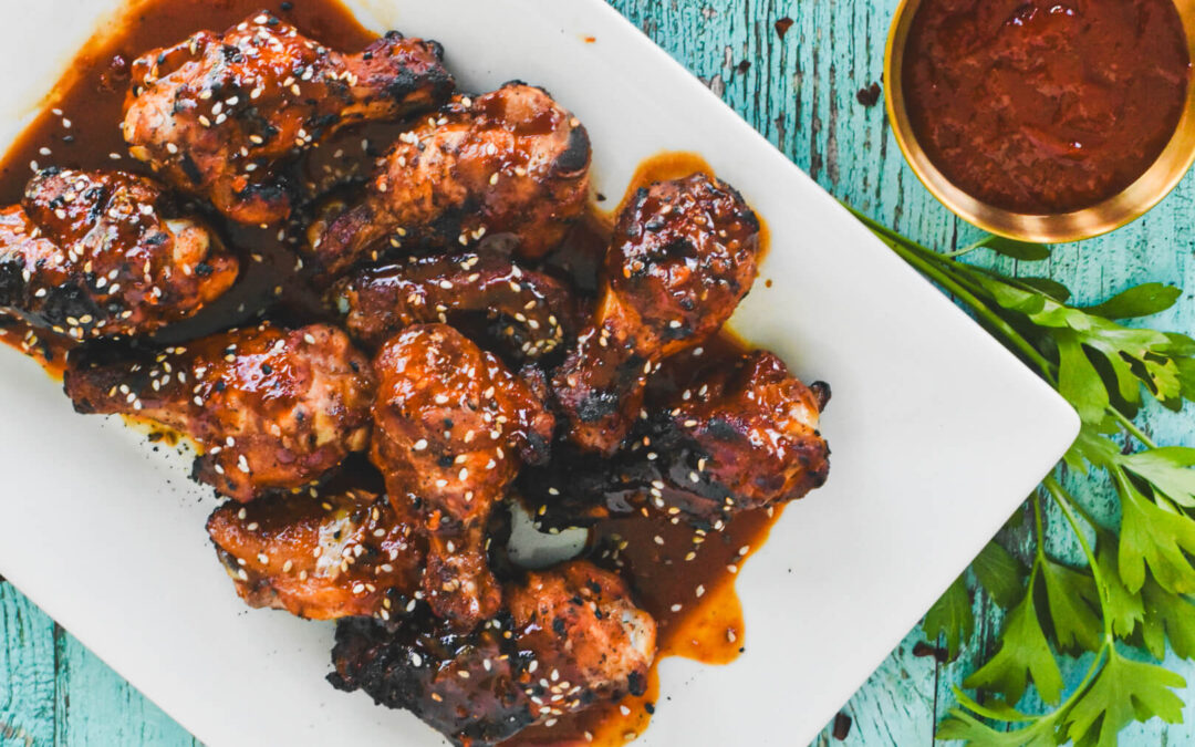 A white platter of gochujang chicken wings topped with white sesame seeds.