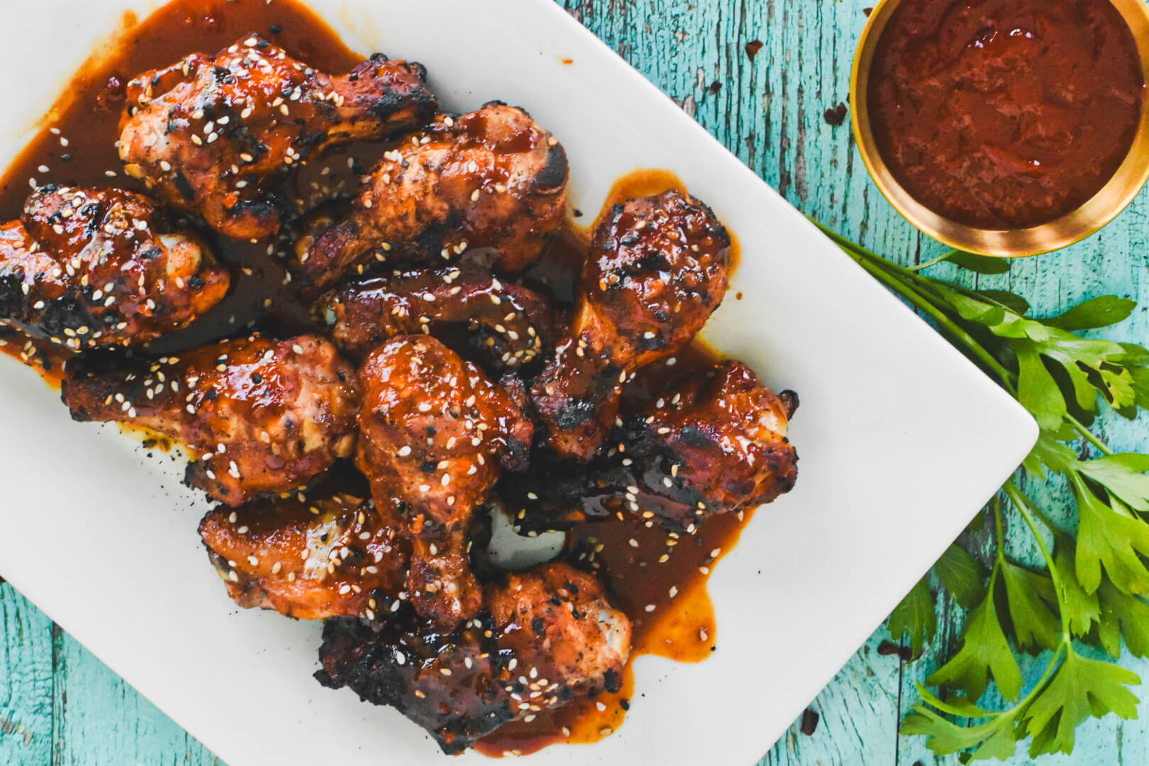 A white platter of gochujang chicken wings topped with white sesame seeds.