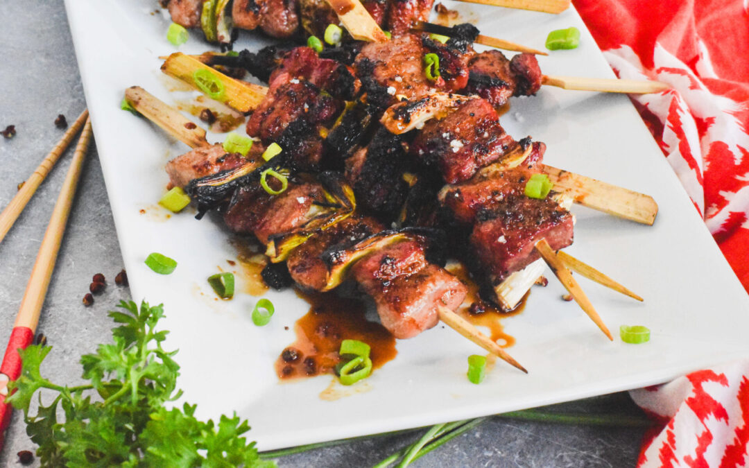 Pork belly skewers on a white platter topped with scallions.