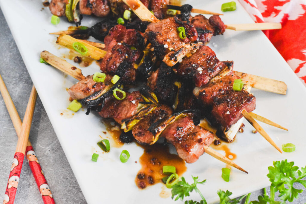 A platter of grilled pork belly skewers topped with scallions.