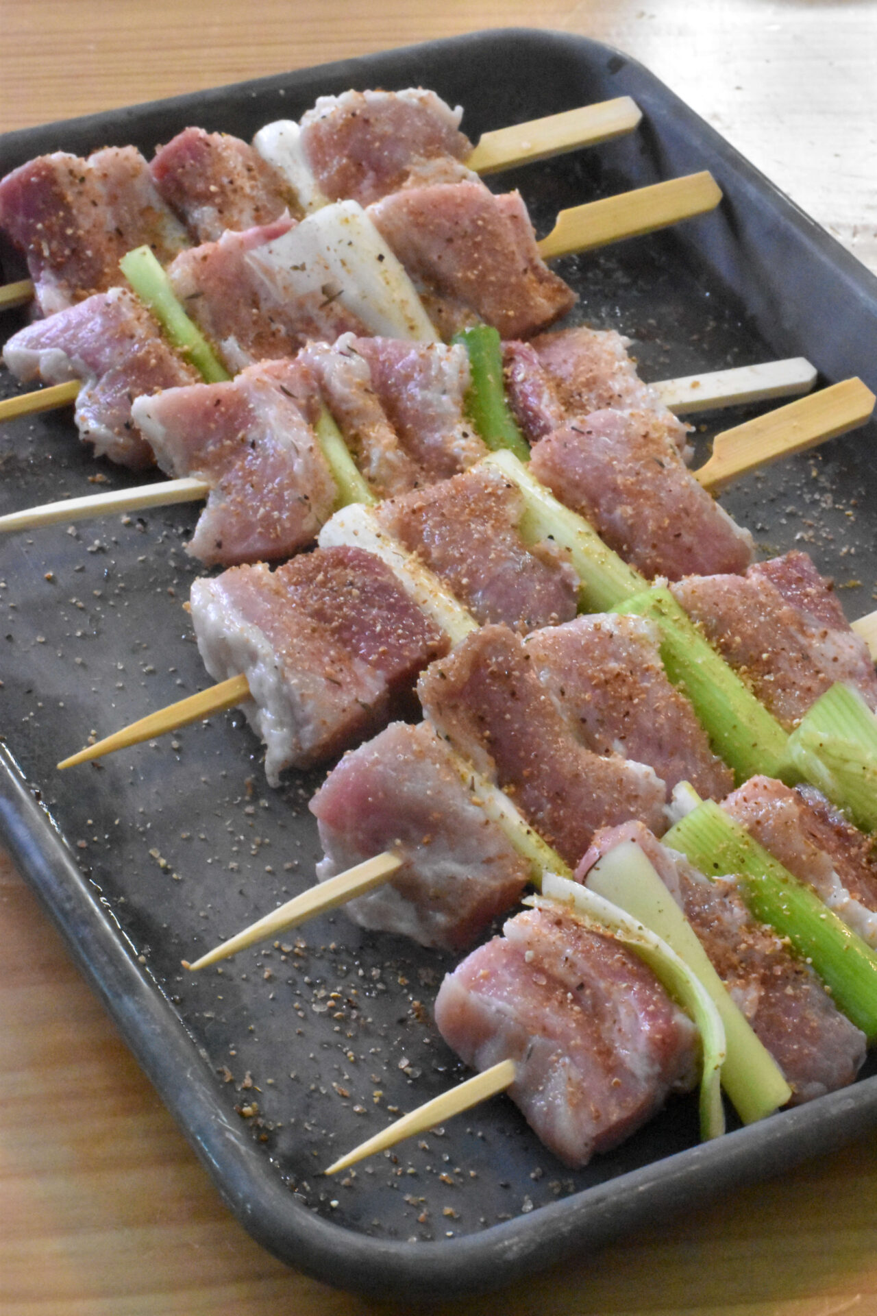 Raw pork belly skewers on a baking dish.