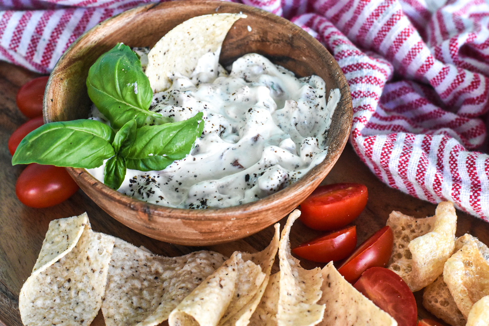 blt dip in wooden bowl on platter with red and white dish towel and tortilla chips and pork rinds for low carb eaters